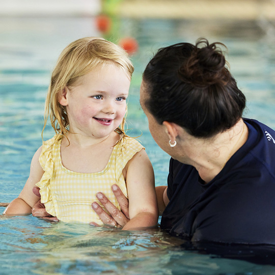 AKAC swim school instructor with smiling little girl in water